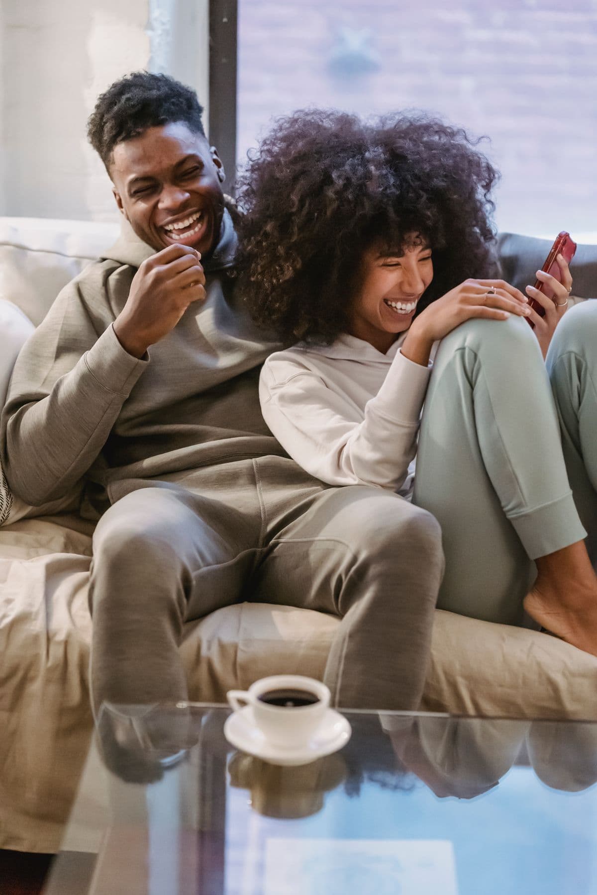 Casal sorrindo junto no sofá enquanto organiza as finanças pelo celular