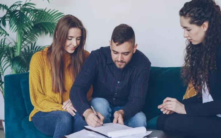 Casal jovem assinando documentos financeiros com a orientação de um consultor.