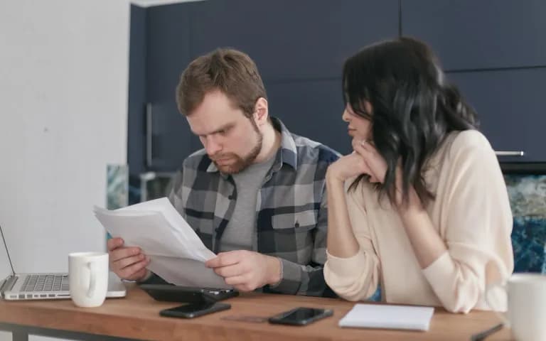 Couple at the kitchen table reviewing a printed agreement together, calm and focused expressions.