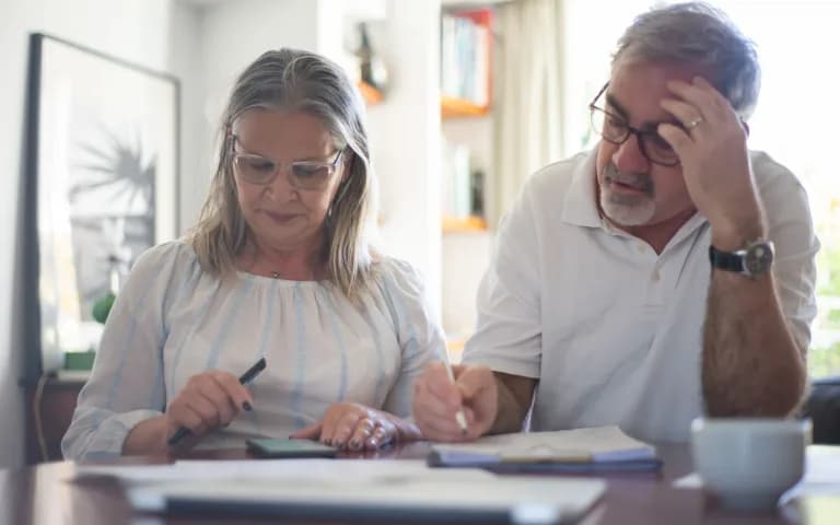 Casal de mais idade fazendo anotações e organizando despesas em casa.