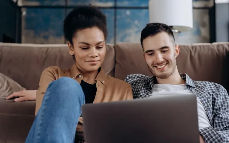 Casal relaxado no sofá de casa, acessando o aplicativo do banco juntos pelo notebook.
