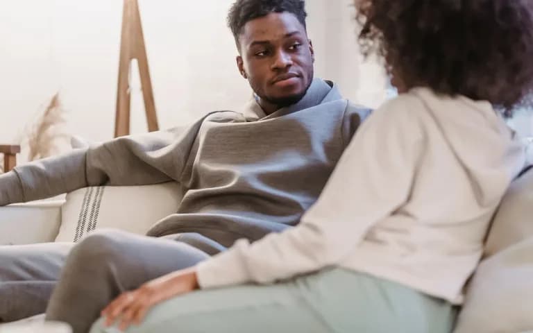 Casal relaxado no sofá de casa, roupas confortáveis, em conversa tranquila e afetuosa.