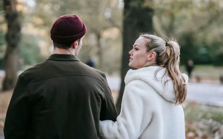 Couple strolling through a park in autumn, deep in conversation, wrapped in warm coats.