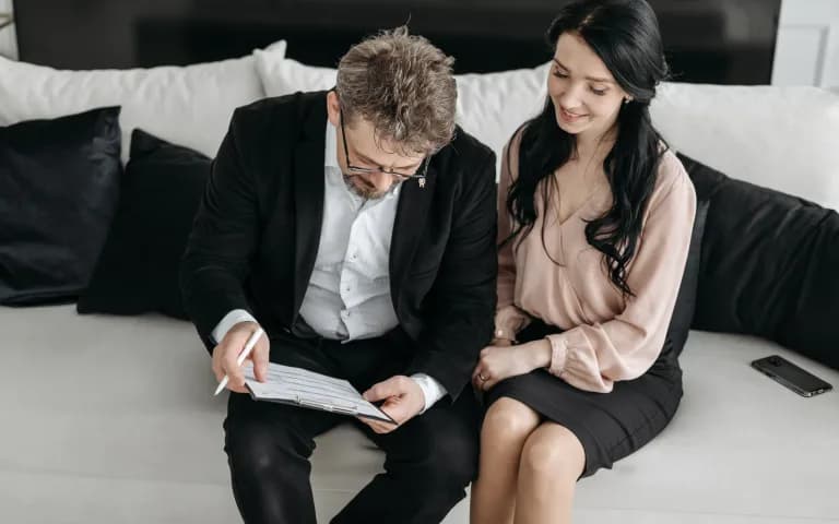 Casal revisando documentos juntos no sofá, em clima sério de trabalho em equipe.